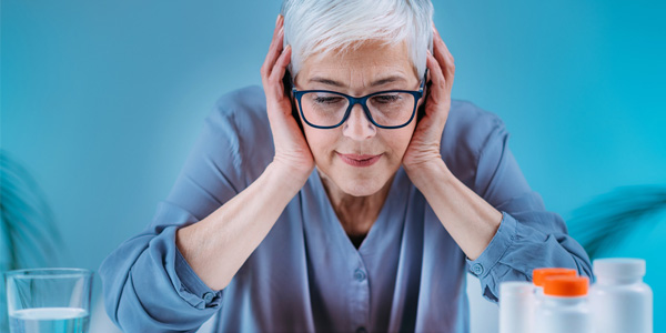 Person sitzt an einem Tisch mit mehreren Medikamentenbehältern und einem Glas Wasser. Szene deutet auf Beratung zur richtigen Einnahme von Medikamenten hin.